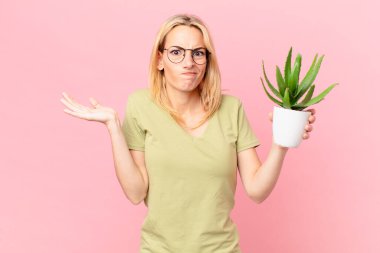 Genç sarışın kadın şaşkın, şaşkın, şüpheci ve elinde bir kaktüs tutuyor.