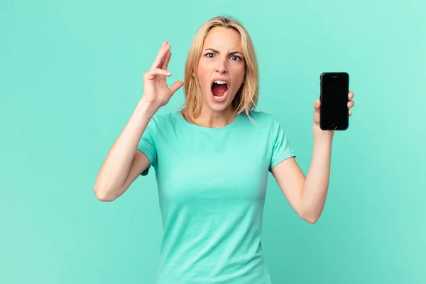 Mujer Rubia Joven Gritando Con Las Manos Alto Sosteniendo Teléfono —  Fotos de Stock