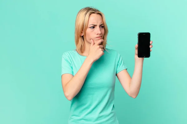 Młoda Blondynka Myśli Czuje Wątpliwości Zdezorientowany Trzyma Smartfon — Zdjęcie stockowe