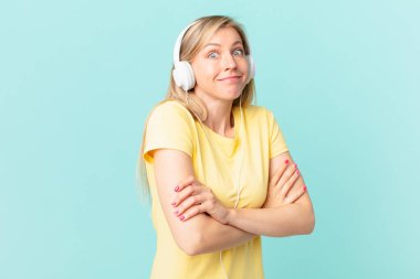 young blonde woman shrugging, feeling confused and uncertain and listening music.