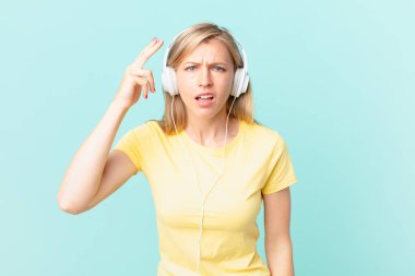 young blonde woman feeling confused and puzzled, showing you are insane and listening music.