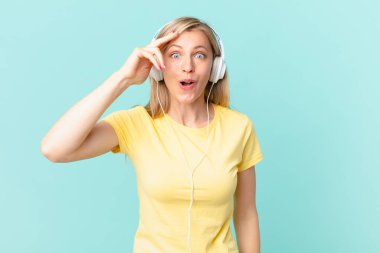 young blonde woman looking happy, astonished and surprised and listening music.