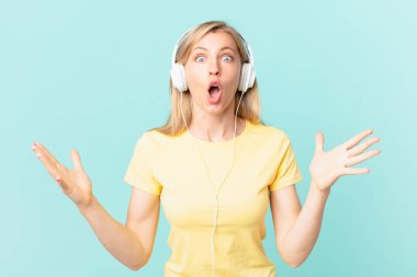 young blonde woman feeling extremely shocked and surprised and listening music.