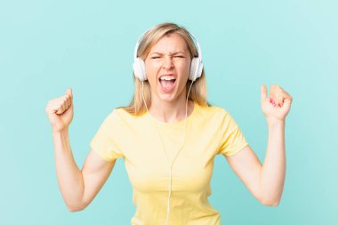 young blonde woman shouting aggressively with an angry expression and listening music.