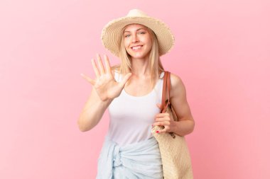Genç sarışın kadın gülümsüyor ve arkadaş canlısı görünüyor, beş numarayı gösteriyor. yaz konsepti