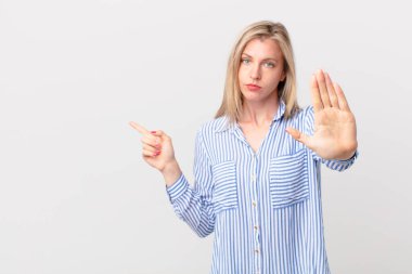 Genç sarışın kadın ciddi görünüyor. Avuç içini gösteriyor. Durdurma hareketi yapıyor.