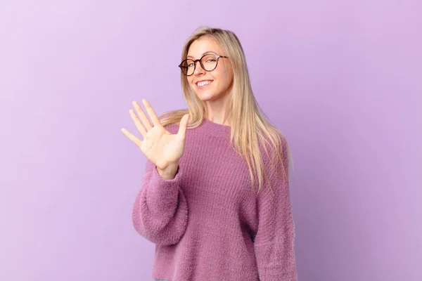 若いブロンドの女性は笑顔で友好的に見え5番目を示し — ストック写真