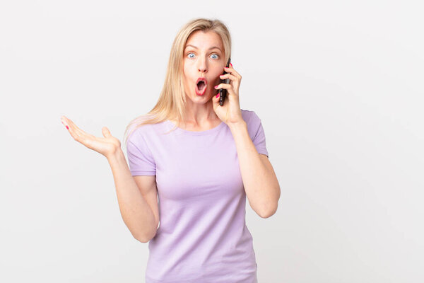 young blonde woman amazed, shocked and astonished with an unbelievable surprise and calling with a smart phone