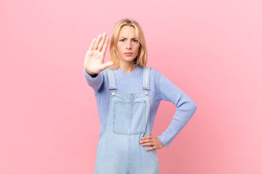 Genç sarışın kadın ciddi görünüyor. Avuç içini gösteriyor. Durdurma hareketi yapıyor.