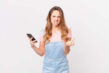 Güzel bir kadın sinirli, sinirli ve hayal kırıklığına uğramış görünüyor ve elinde bir akıllı telefon tutuyor.