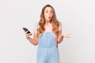 Güzel bir kadın şok olmuş, şaşırmış ve elinde akıllı bir telefon tutuyor.