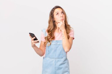 Düşünen, kuşkulu, kafası karışık ve elinde akıllı bir telefon tutan güzel bir kadın.