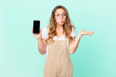 Güzel bir kadın şaşkın, şaşkın, şüpheci ve elinde bir akıllı telefon tutuyor.