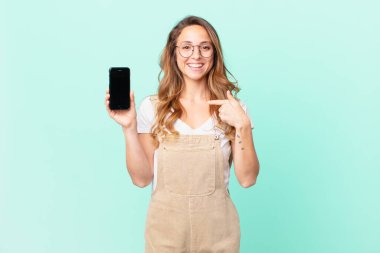 Güzel bir kadın kendini mutlu hissediyor ve heyecanlı ve akıllı bir telefonla kendini işaret ediyor.
