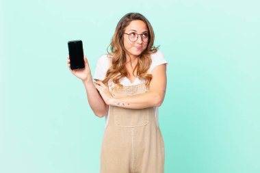 Güzel bir kadın omuz silkiyor, kafası karışık ve kararsız ve elinde akıllı bir telefon tutuyor.