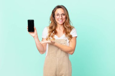 Güzel bir kadın neşeyle gülümsüyor, mutlu hissediyor ve bir konsept gösteriyor ve akıllı bir telefon tutuyor.