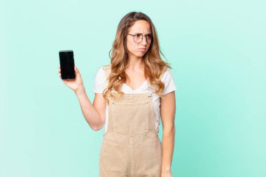 Güzel bir kadın üzgün, üzgün ya da kızgın ve yana bakıyor ve elinde bir akıllı telefon tutuyor.