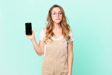 Şaşkın, kafası karışmış ve elinde akıllı bir telefon tutan güzel bir kadın.