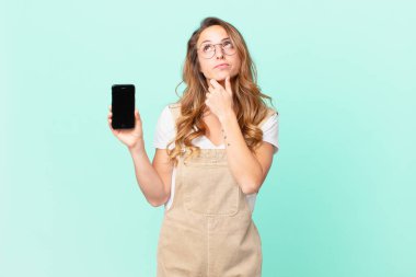 Düşünen, kuşkulu, kafası karışık ve elinde akıllı bir telefon tutan güzel bir kadın.