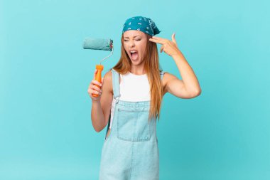 Güzel bir kadın mutsuz ve stresli görünüyor, intihar jesti silah işareti yapıyor yeni bir ev duvarı boyuyor