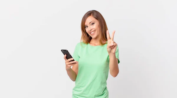 Pretty Woman Smiling Looking Friendly Showing Number Two Using Smartphone — Stock Photo, Image