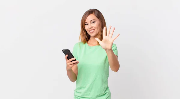 Pretty Woman Smiling Looking Friendly Showing Number Five Using Smartphone — Stock Photo, Image