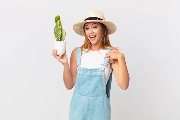 Ładna Kobieta Czuje Się Szczęśliwy Wskazując Siebie Podekscytowany Trzymając Kaktusa — Zdjęcie stockowe