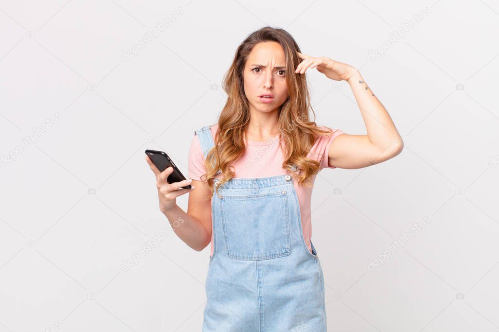 pretty woman feeling confused and puzzled, showing you are insane and holding a smartphone
