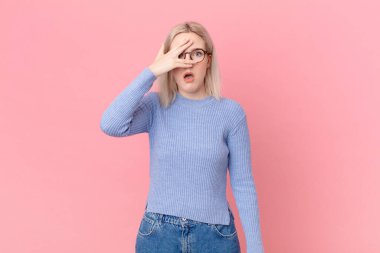 Sarışın, güzel bir kadın. Şok olmuş, korkmuş ya da korkmuş görünüyor.