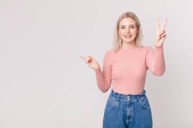 Güzel sarışın kadın gülümsüyor ve mutlu görünüyor, zafer ya da barış işareti yapıyor.