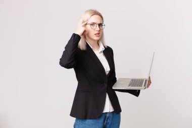 Sarışın, güzel bir kadın şaşkın ve şaşkın hissediyor, deli olduğunu ve elinde dizüstü bilgisayar tuttuğunu gösteriyor.