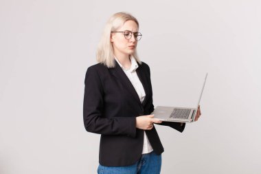 Sarışın, güzel bir kadın üzgün, üzgün ya da kızgın hissediyor ve yan tarafa bakıyor ve elinde bir laptop tutuyor.