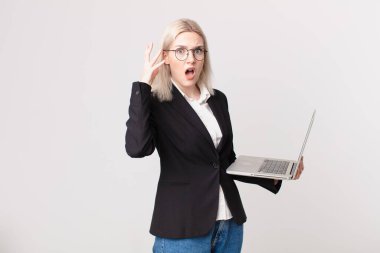 Sarışın, güzel bir kadın ellerini havaya kaldırıp bağırıyor ve dizüstü bilgisayarını tutuyor.