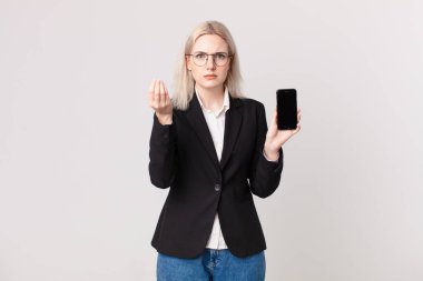 Sarışın, güzel bir kadın kapiş ya da para hareketi yapıyor. Sana ödemeni söylüyor ve elinde bir cep telefonu tutuyor.