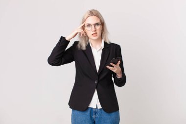 Sarışın, güzel bir kadın şaşkın ve şaşkın hissediyor, deli olduğunu ve elinde cep telefonu tuttuğunu gösteriyor.