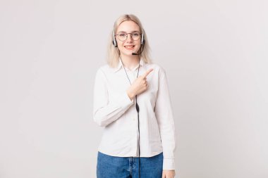 Sarışın, güzel bir kadın neşeyle gülümsüyor, mutlu hissediyor ve tele pazarlama konseptini işaret ediyor.