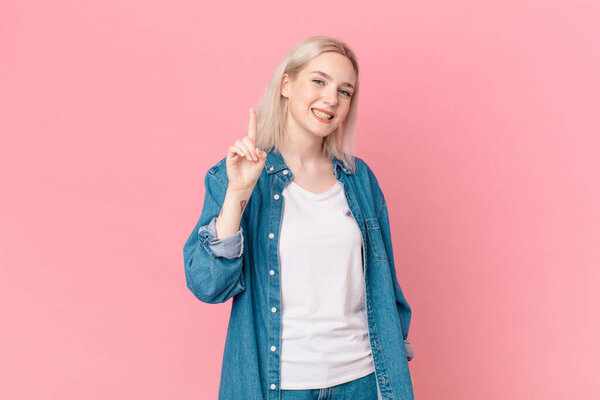 Красивая женщина улыбается и выглядит дружелюбно, показывая номер один