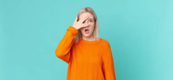 stock image blond pretty woman looking shocked, scared or terrified, covering face with hand