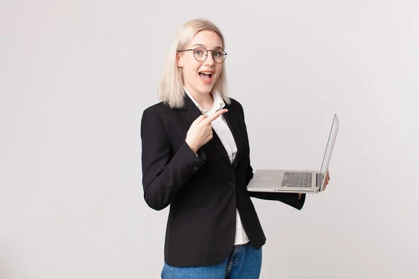 Blondynka Ładna Kobieta Wygląda Podekscytowany Zaskoczony Wskazując Bok Trzymając Laptopa — Zdjęcie stockowe