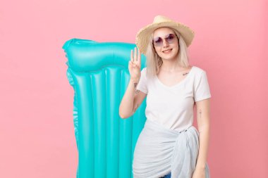 Sarışın, güzel bir kadın gülümsüyor ve arkadaş canlısı görünüyor, üç numarayı gösteriyor. yaz konsepti