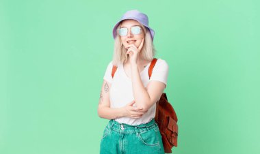 Sarışın, güzel bir kadın mutlu bir şekilde gülümsüyor ve hayal kuruyor ya da şüphe ediyor. yaz konsepti