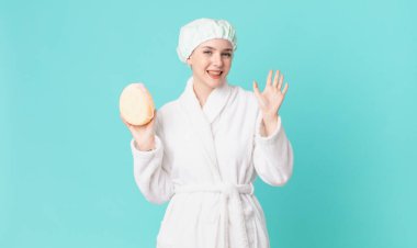 Sarışın, güzel bir kadın mutlu bir şekilde gülümsüyor, el sallıyor, seni selamlıyor ve bornoz giyiyor.