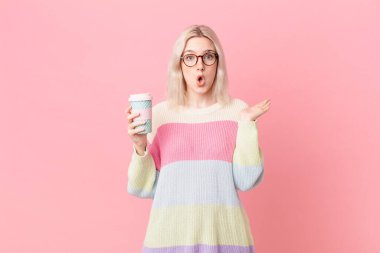 blond pretty woman looking surprised and shocked, with jaw dropped holding an object. coffee concept