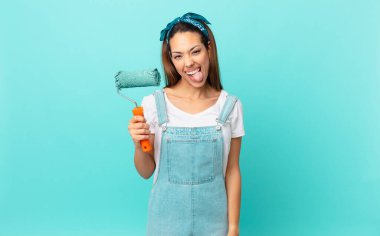 young hispanic woman with cheerful and rebellious attitude, joking and sticking tongue out and painting a wall