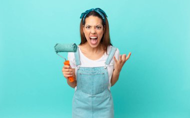young hispanic woman looking angry, annoyed and frustrated and painting a wall