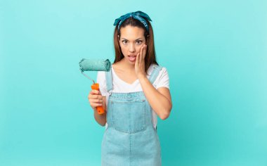 young hispanic woman feeling shocked and scared and painting a wall