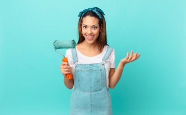 young hispanic woman feeling happy, surprised realizing a solution or idea and painting a wall