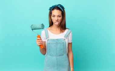 young hispanic woman feeling disgusted and irritated and tongue out and painting a wall