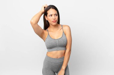 Genç İspanyol kadın şaşkın ve kafası karışık, kaşınan bir kafa hissediyor. fitness konsepti