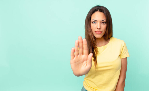 молодая латиноамериканка, выглядящая серьезной, показывающая открытую ладонь.